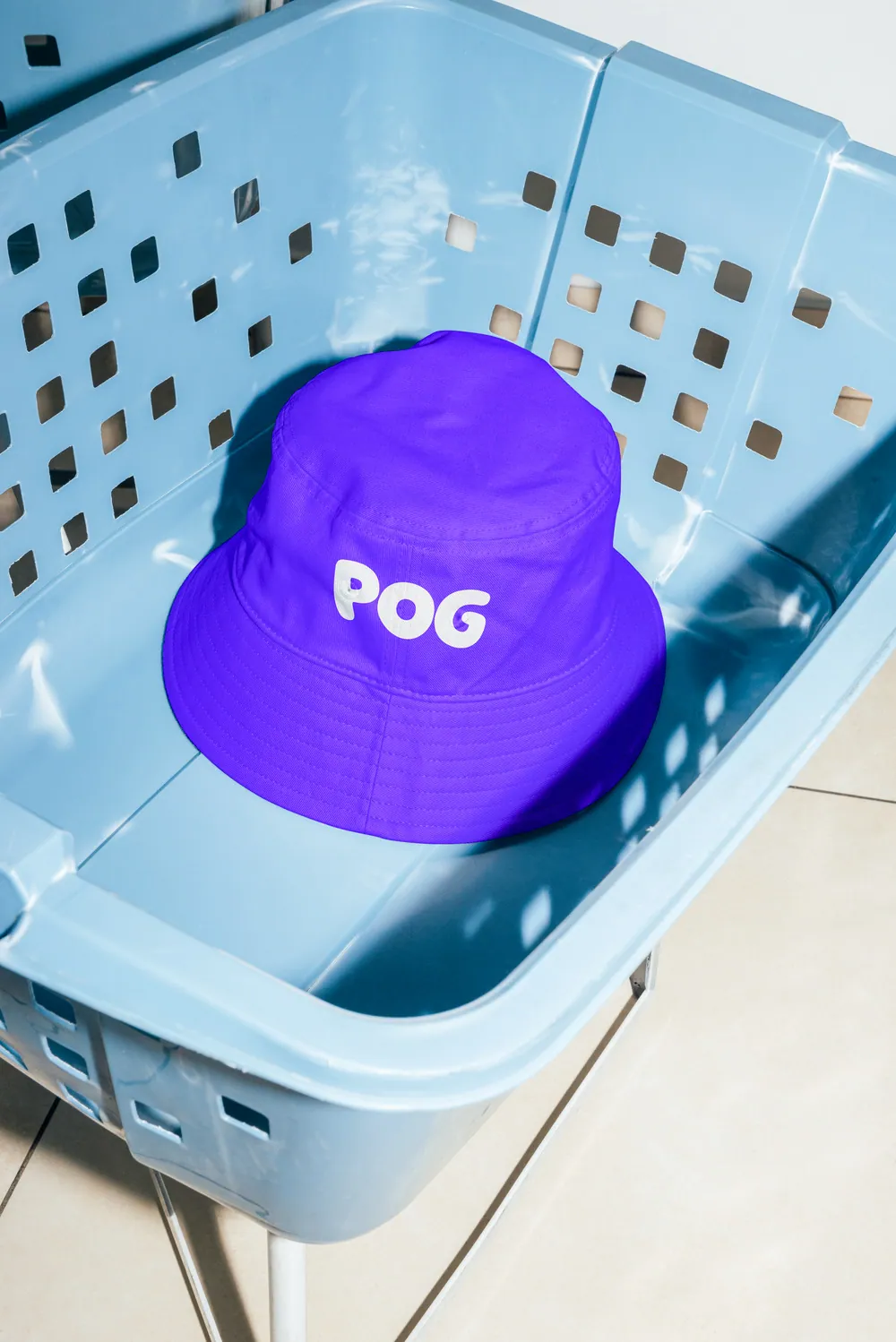 Violet bucket hat with the POG wordmark in a laundry basket